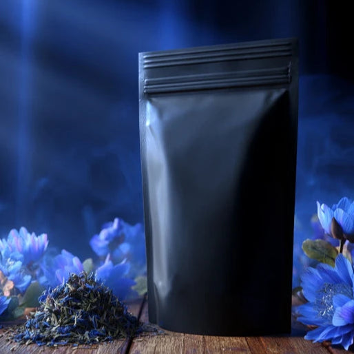 Black packaging pouch on a wooden surface with blue flowers and dried herbs.